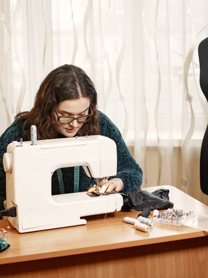 Fabric in a typewriter. Woman deftly works with a sewing machine. Woman with glasses.